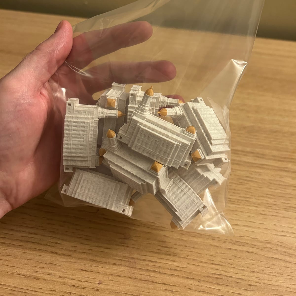 Ten tiny 2in Smithfield Utah Temple statues in a clear bag, held in one hand