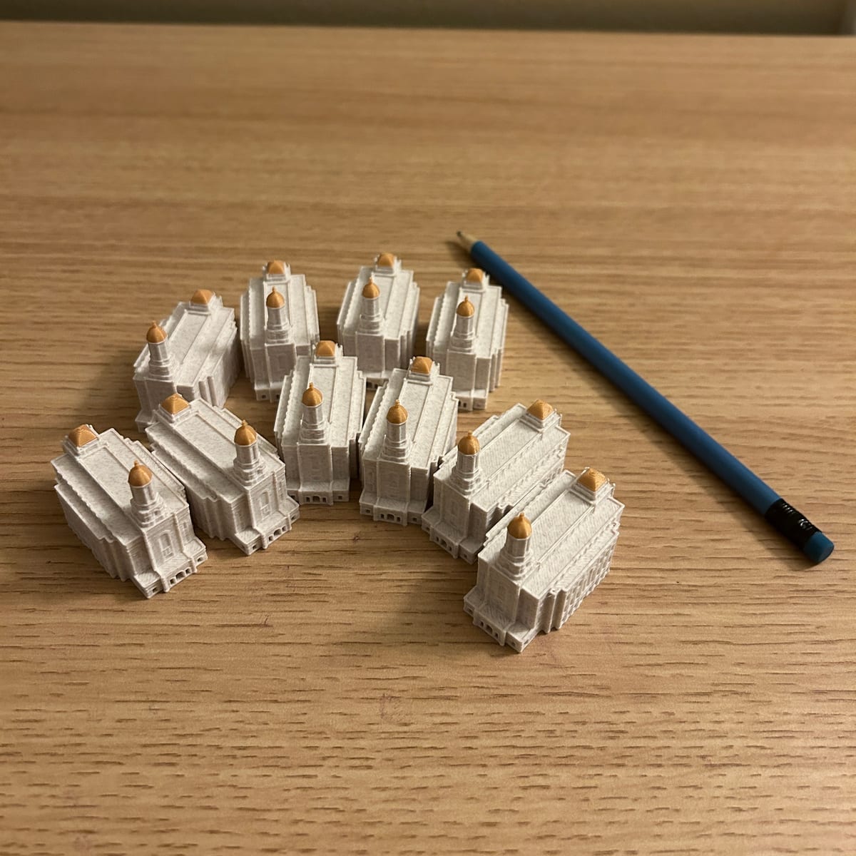 Ten tiny 2in Smithfield Utah Temple statues laid out on a table beside a pencil for scale